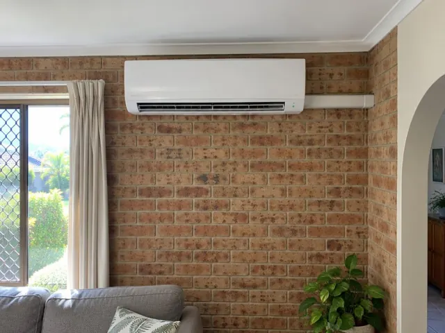White split system mounted high on a brick living room wall above curtains and sofa in Carrara