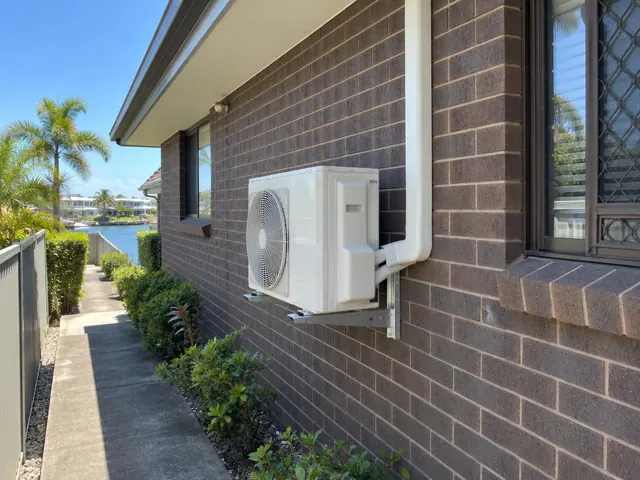 Wall-mounted outdoor air conditioner unit on brick house beside a canal in Broadbeach Waters