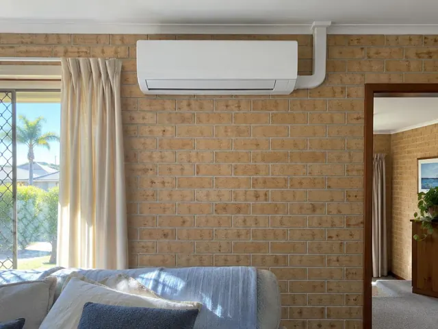 Wall-mounted split system above a brick feature wall in a carpeted living room in Merrimac